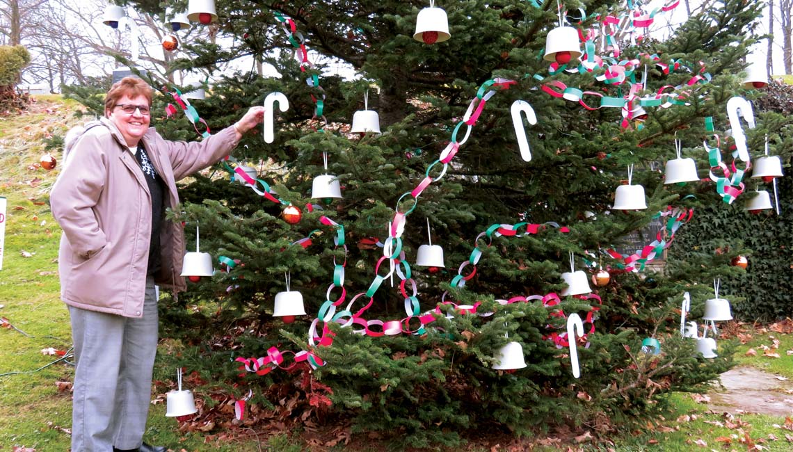 Martha Starkey hangs a decorative candy cane on the Christmas tree at the tomb of August Imgard.