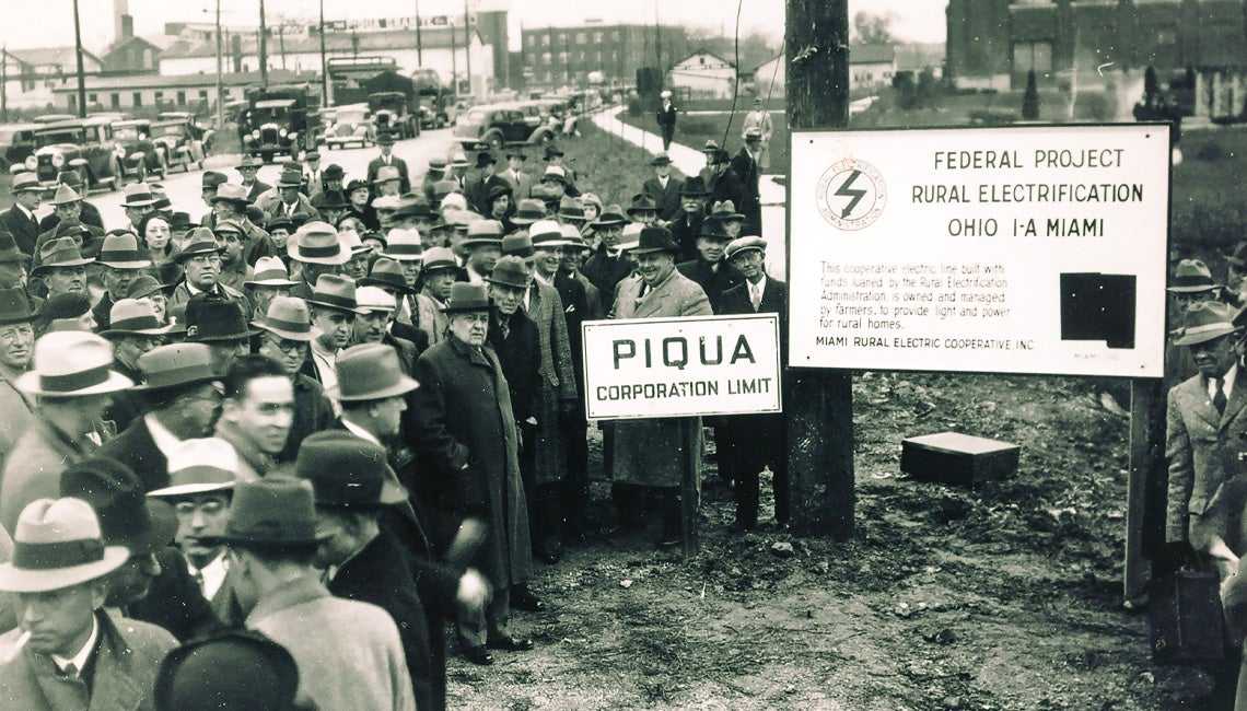 A black and white photo of Ohioans watching the setting of a utility pole