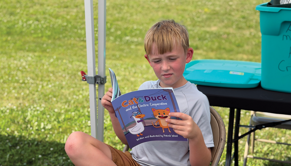 A young boy sitting on a chair outside reading a book called Cat & Duck