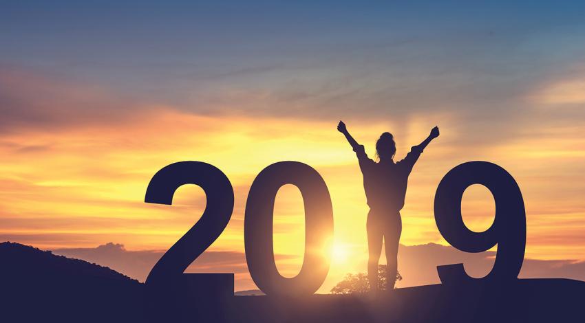 A woman stands as the "1" in 2019 against a sunset.