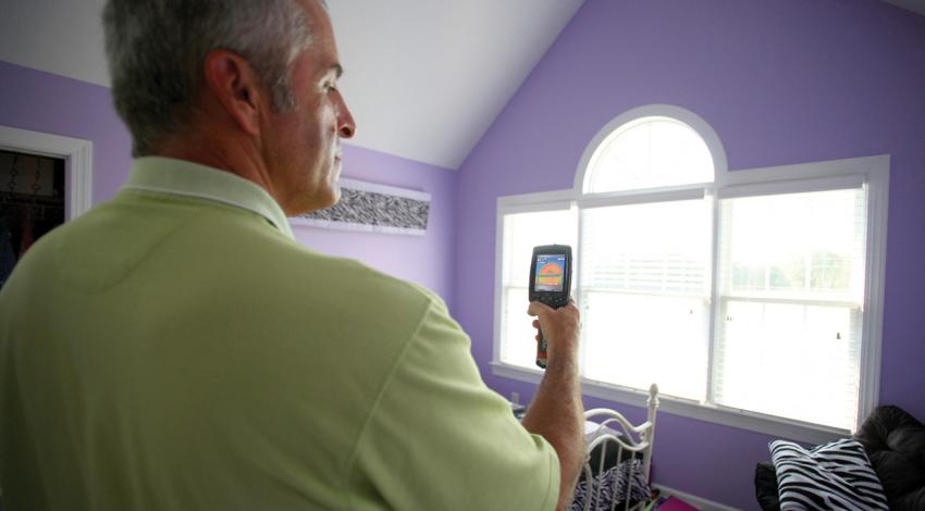An energy auditor uses an infrared camera to look for areas around the window that are leaky or poorly insulated.