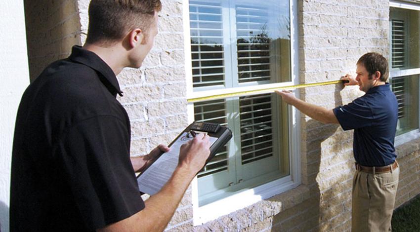 A man measures a window while another records the measurements.