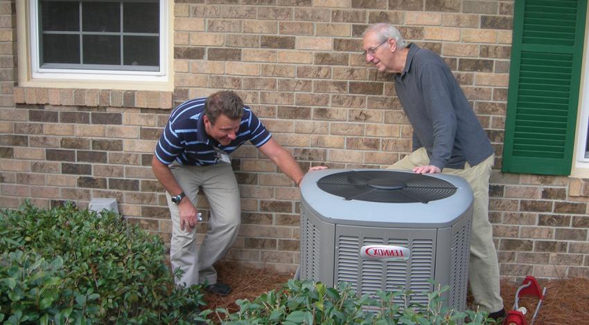 Two men look at an outdoor AC unit