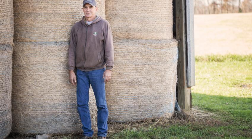 Roger Rhonemus poses for a picture next to a stack of haybales. 