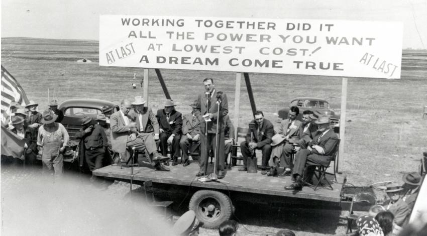 A black and white photo of a group of men on a makeshift stage advertising power.