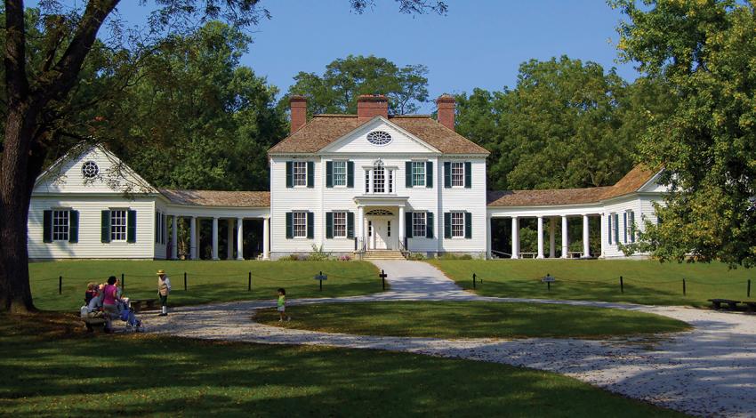 A large, sprawling white house is pictured surrounded by greenery.