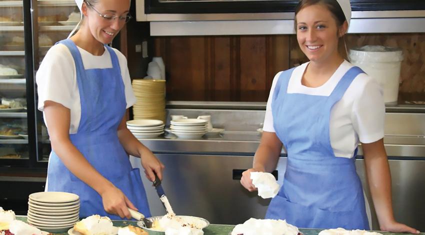 Two women making pies pose for a picture.