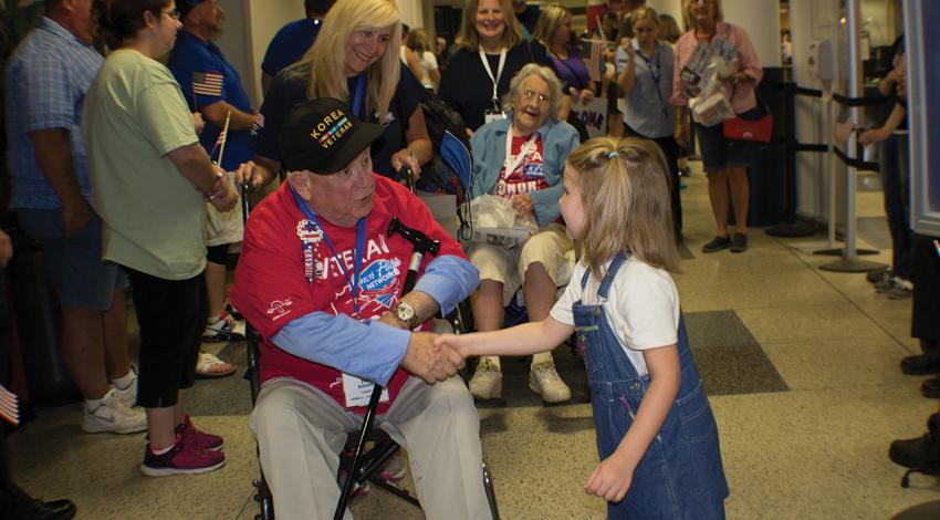 A young girl shakes the hand of a male veteran.