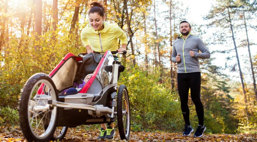 A couple jogs while pushing a child in a stroller