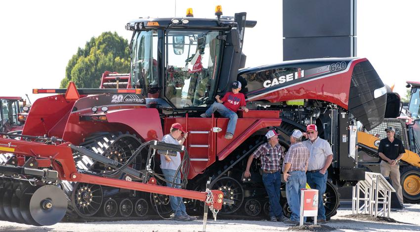 A few men stand around a giant red tractor while a child sits on the side of it.