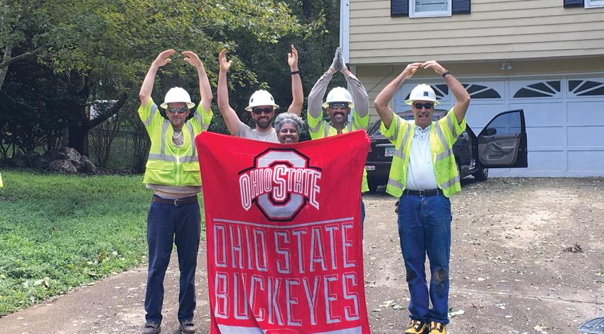 Linemen spell OHIO with their arms and surround a woman holding an Ohio State Buckeyes banner.