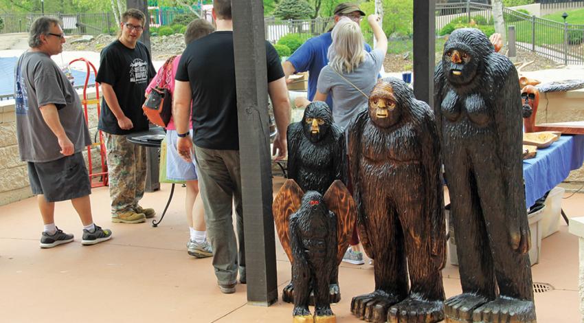 A group of people stand next to multiple statues of Bigfoot.