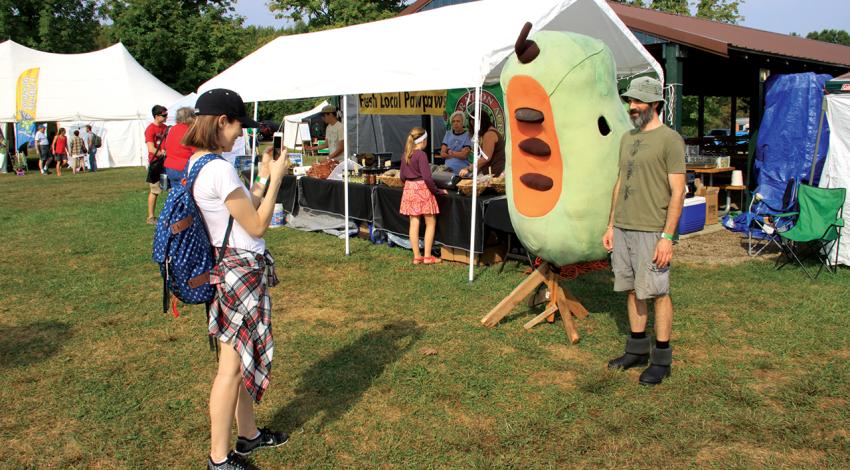 A girl takes a picture of someone next to a pawpaw mascot.-