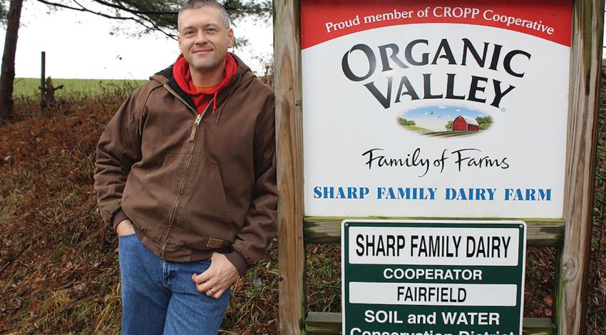 Kyle Sharp poses next to his family farm's sign.