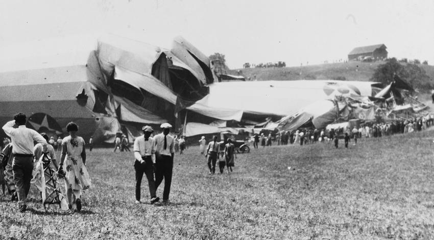 A crowd stands around the crashed ship staring at the wreckage.