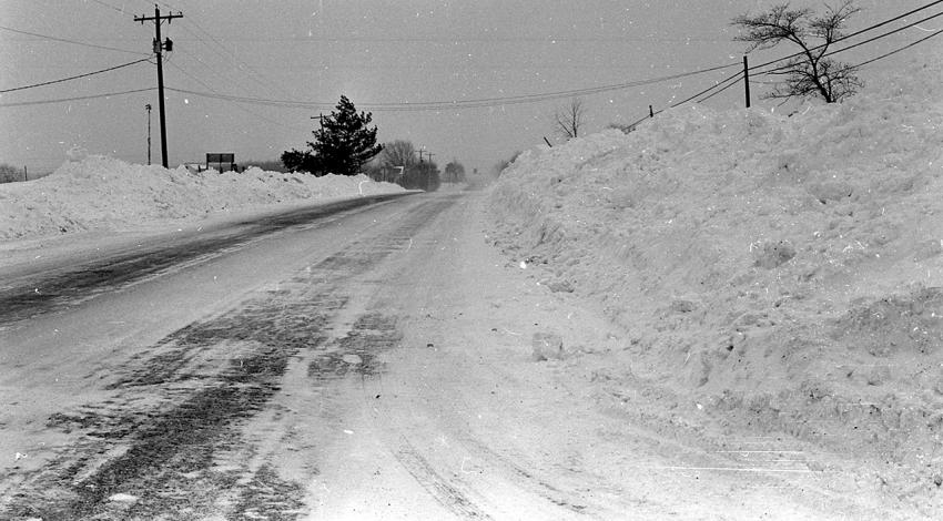 A snow-covered road with large piles of snow on either side of it.