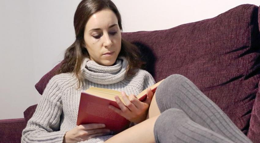 A woman reads a book on a couch.