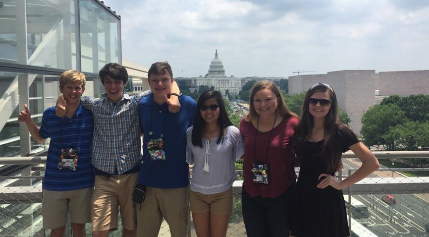 A group of kids smiles in front of the U.S. Capitol Building.