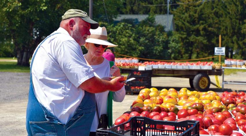 In his signature bib overalls and white shirt, Lee Jones slices open an heirloom tomato for customer Mara Ghafari.