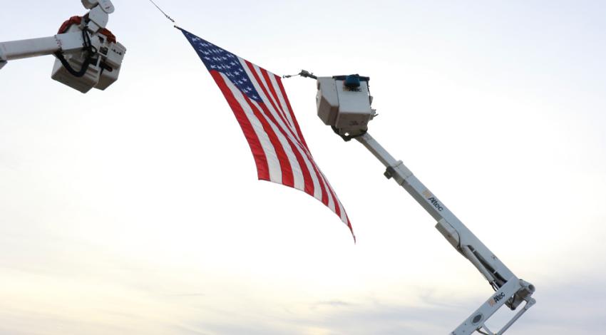 An American flag being held by two bucket trucks
