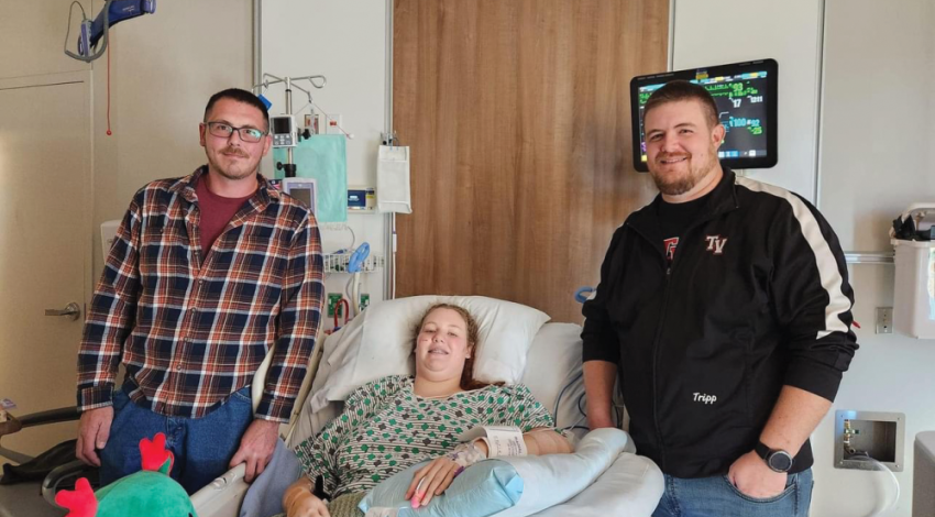 A young girl in a hospital bed beside the two men who saved her life