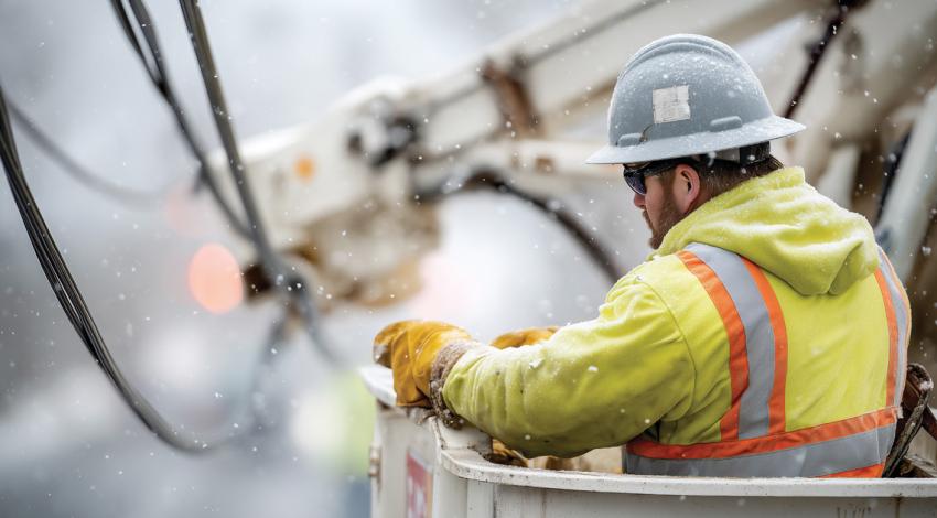 A lineworker in the cradle of a bucket truck working in the snow
