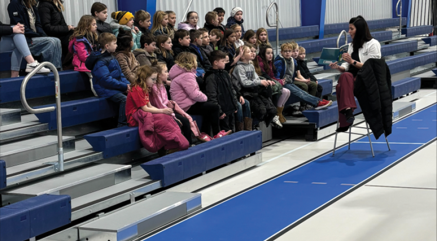 A woman reading a book to a group of young children in a school gymnasium