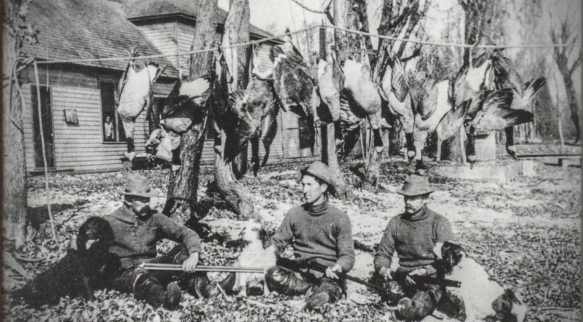 A black and white image of men sitting on the ground with guns after a duck hunt