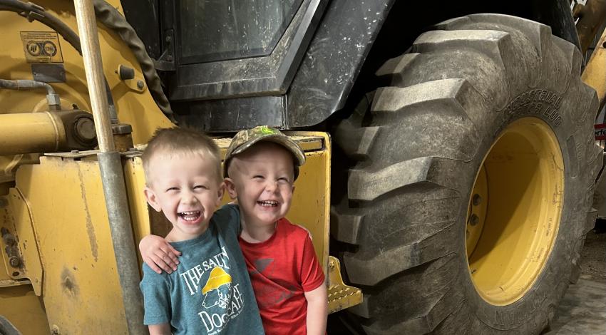 two little boys in front of yellow backhoe