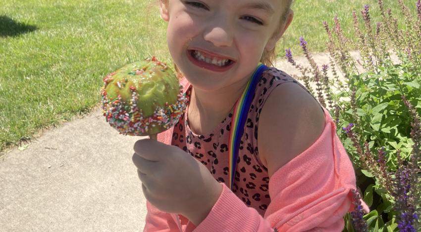 Girl with missing front tooth holds caramel apple with sprinkles