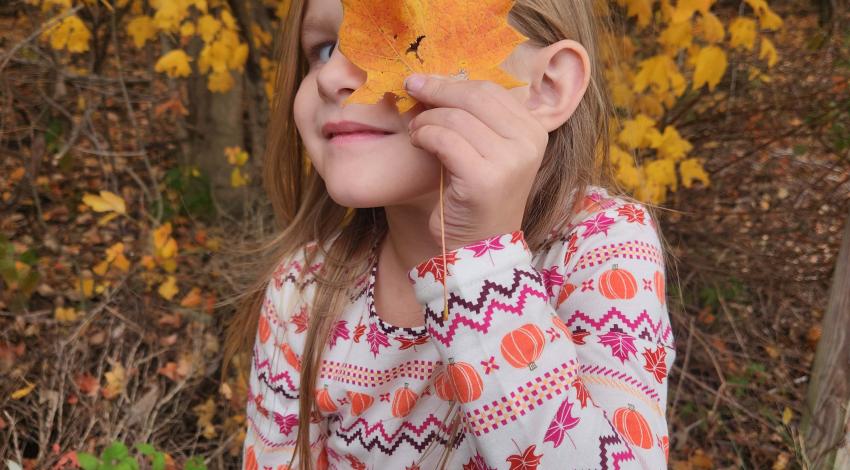 little girl looking through hole in orange leaf