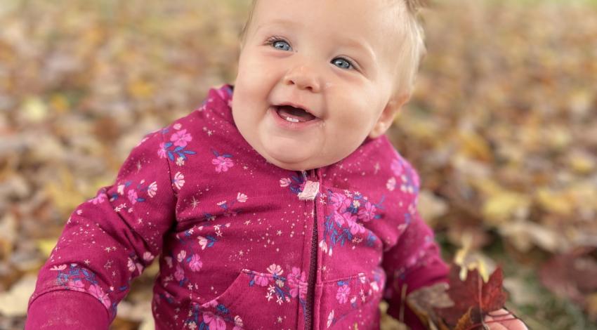 baby in pink jacket sits in leaves
