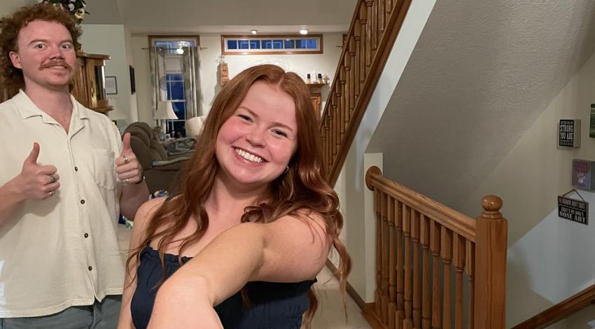 woman shows hand with engagement ring, man in background