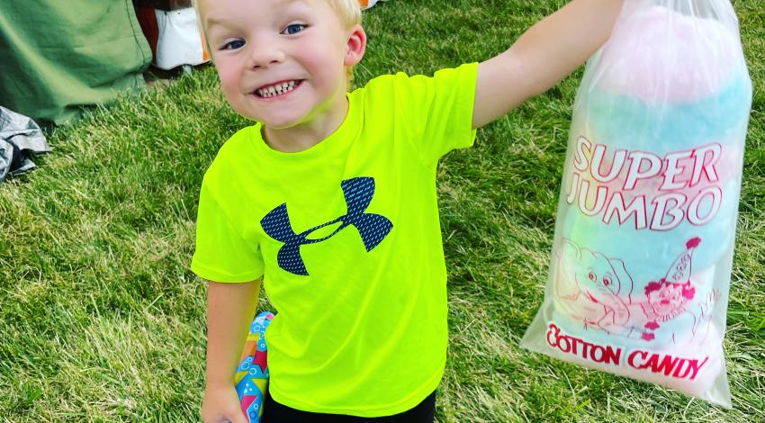 Small boy smiles while holding up a bag of cotton candy