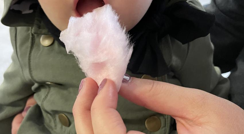 baby in overalls and hat opens up for a bite of pink cotton candy