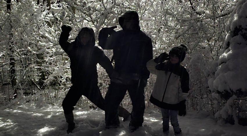 three kids in silhouette in front of snowy trees