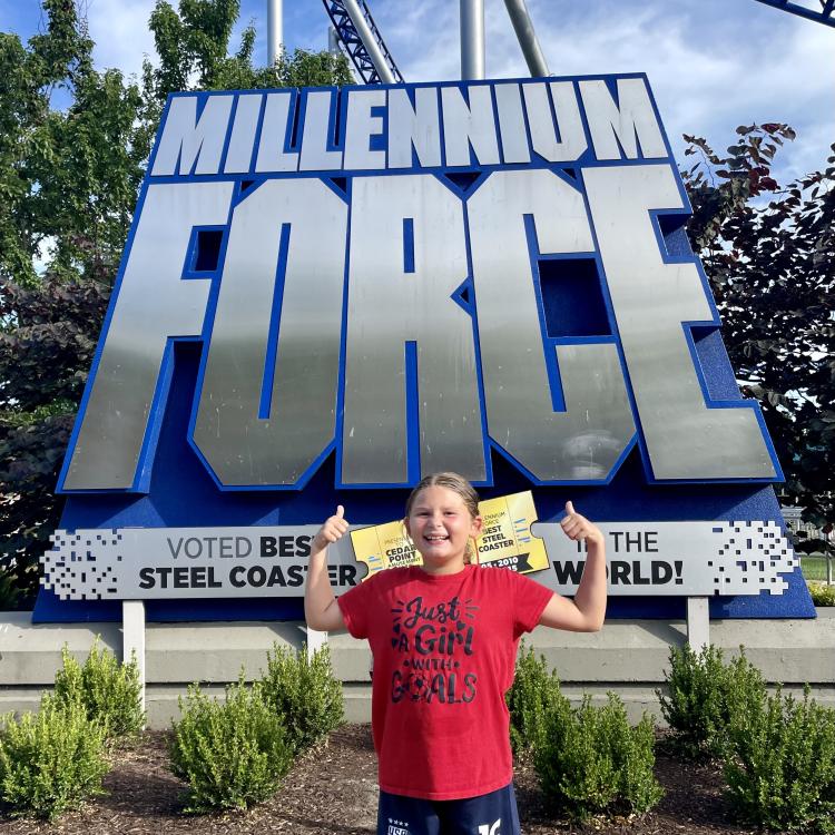kid standing in front of roller coaster sign
