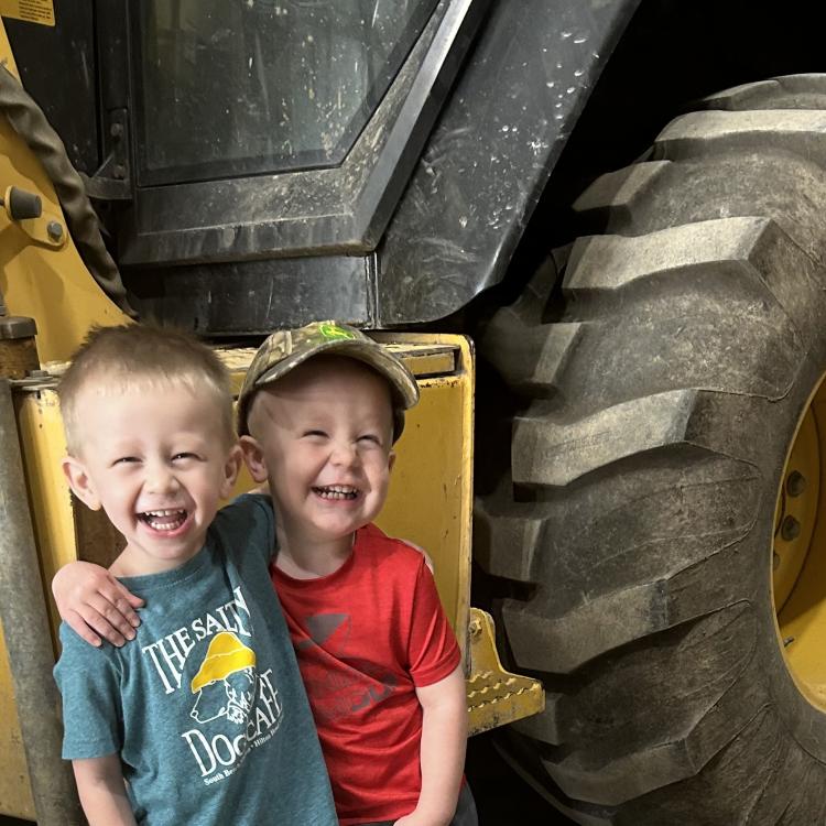 two little boys in front of yellow backhoe
