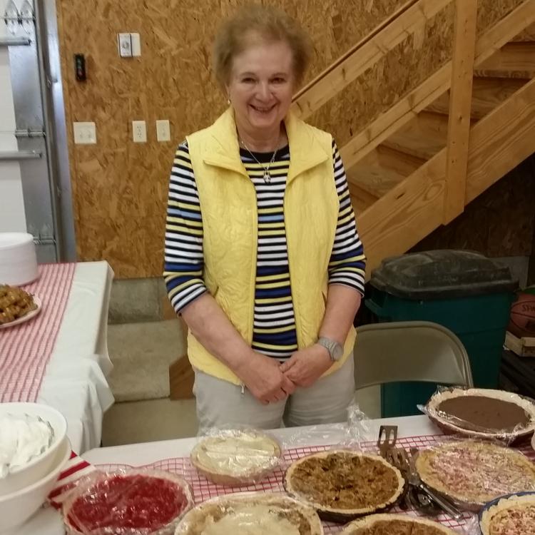 woman stands behind table covered in pies