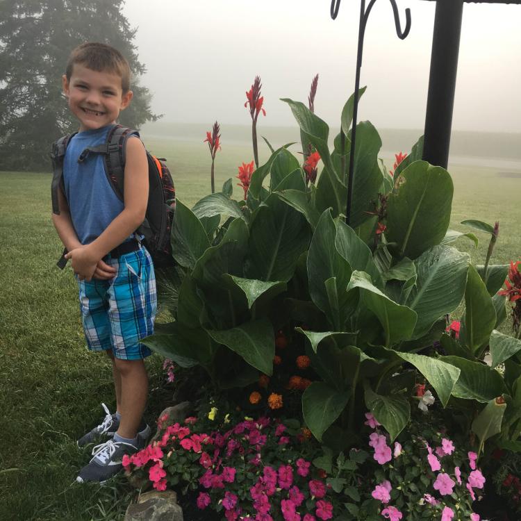 little boy with backpack next to flower bed