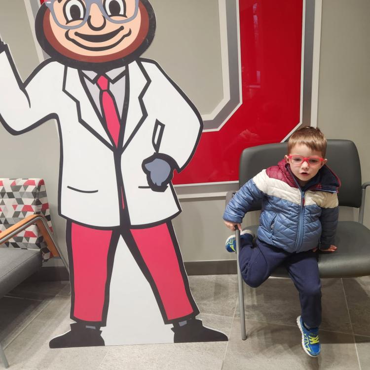little boy next to buckeye mascot cutout - both wearing glasses