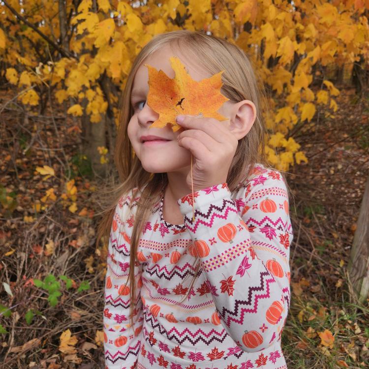 little girl looking through hole in orange leaf
