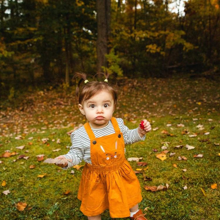 little girl in orange dress in front of fallen leaves