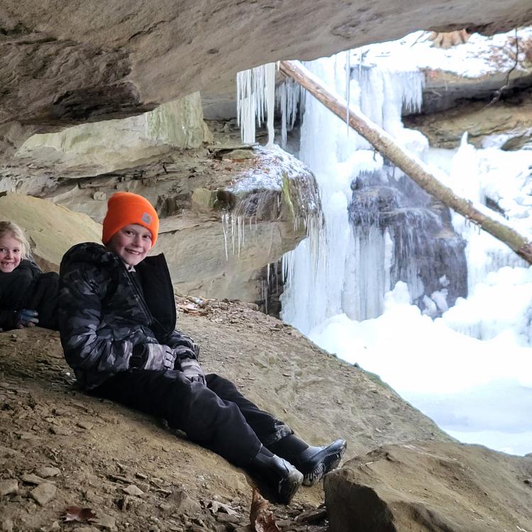 boy and girl sitting in front of frozen waterfall
