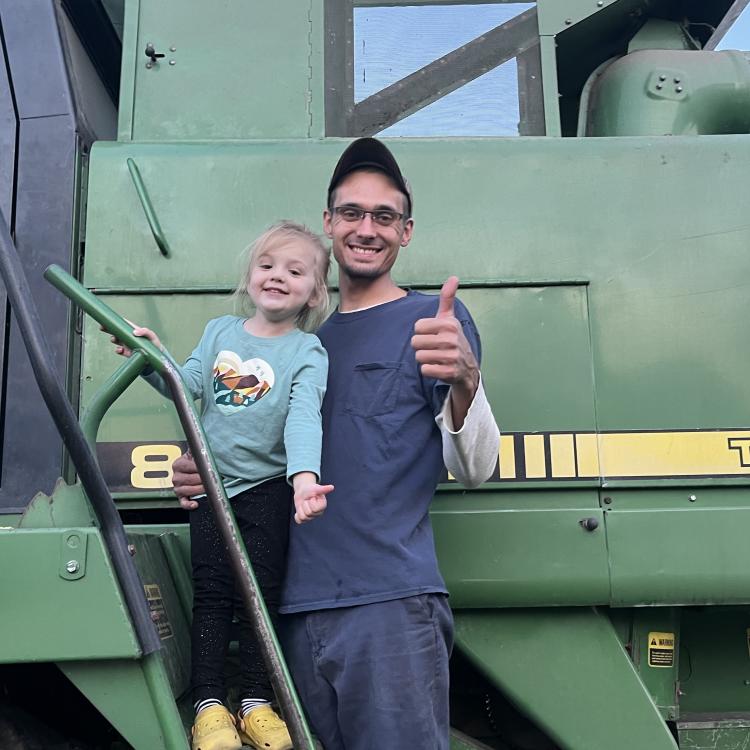 man and small girl in front of green farm machinery