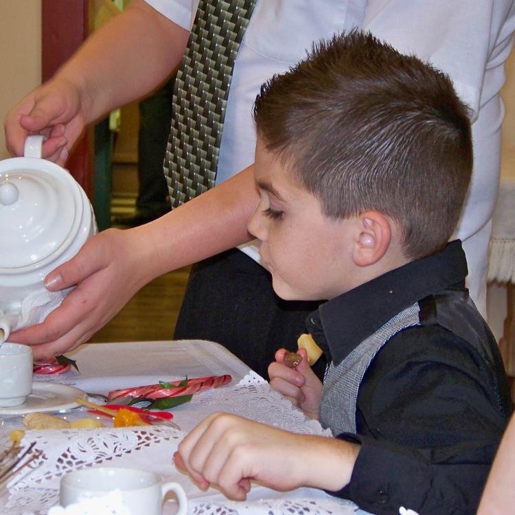 little boy at table, watching as tea is poured into his cup