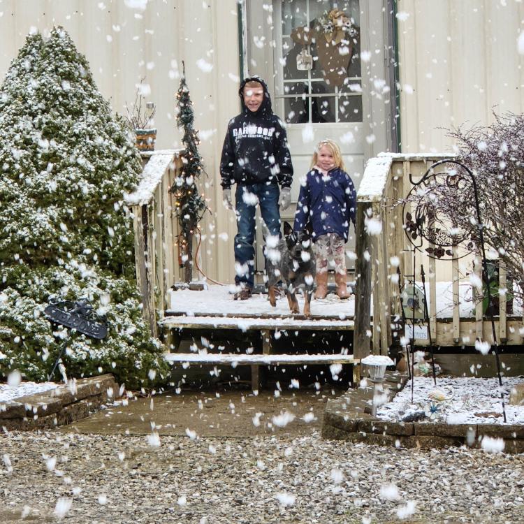two kids and dog on porch with snow falling