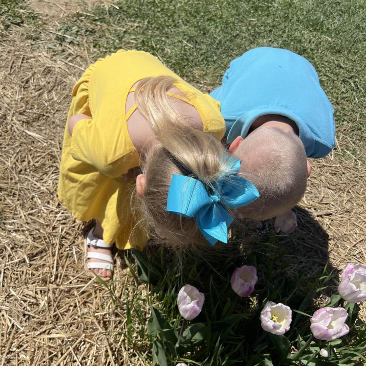 little girl and little boy, bending over to smell flowers