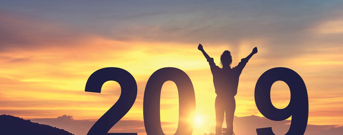 A woman stands as the "1" in 2019 against a sunset.
