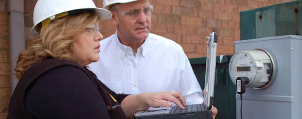 Lisa Queen and Kevin Kemmerer wear hard hats and look at a computer.